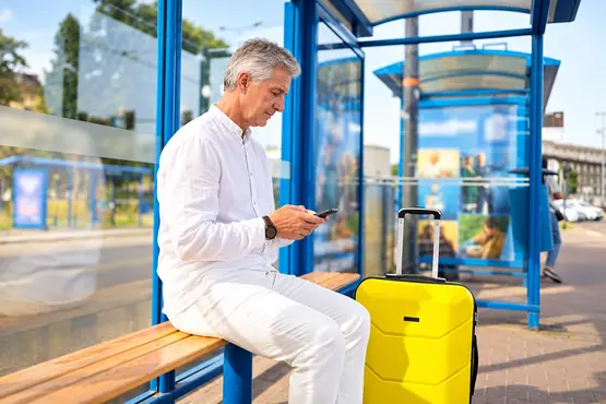 Voyageur assis dans un abri avec son téléphone et une valise jaune, illustration VTC dans le Morbihan