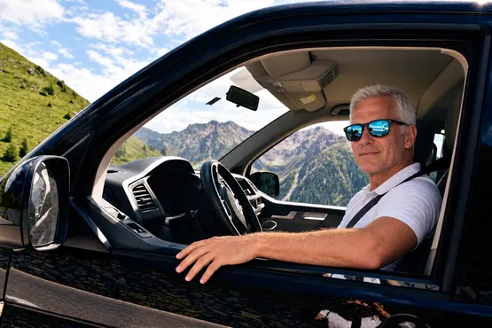 Homme avec des lunettes de soleil au volant d’une voiture en montagne, illustration VTC dans le Puy-de-Dôme