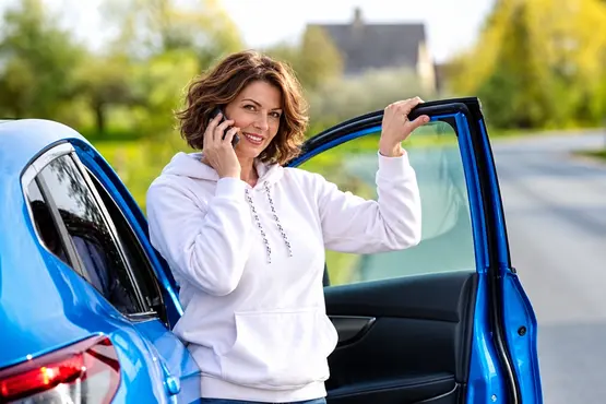 Femme au téléphone près de la portière ouverte d’une voiture bleue, illustration VTC dans le Rhône