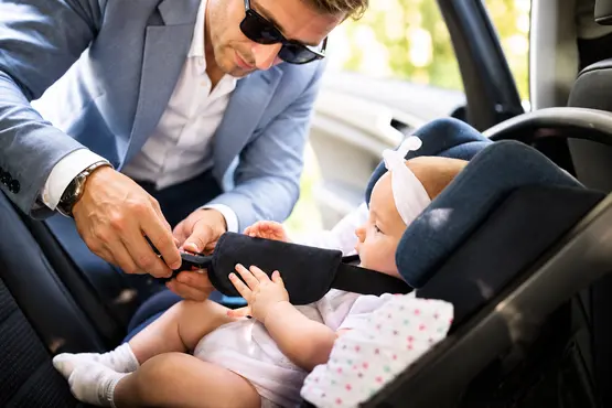 Adulte ajustant le harnais d’un bébé dans un siège auto — illustration VTC : Vendée